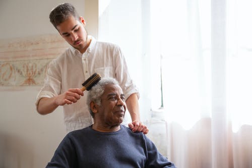 Elder man getting hair brushed by caretaker