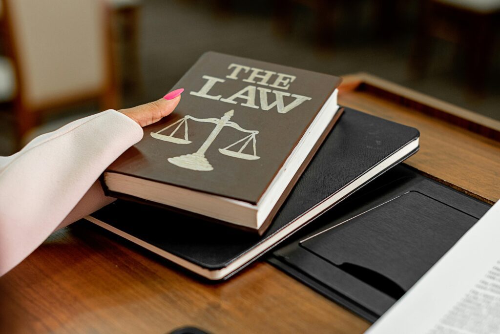 hand holding a book entitled "the Law" with a picture of scales) on a wooden desk. 