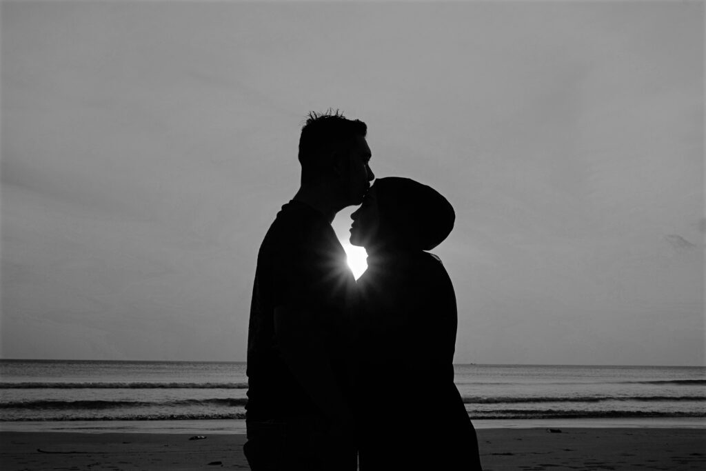 Man and woman embracing. The sun is between their profiles and the background is the ocean
