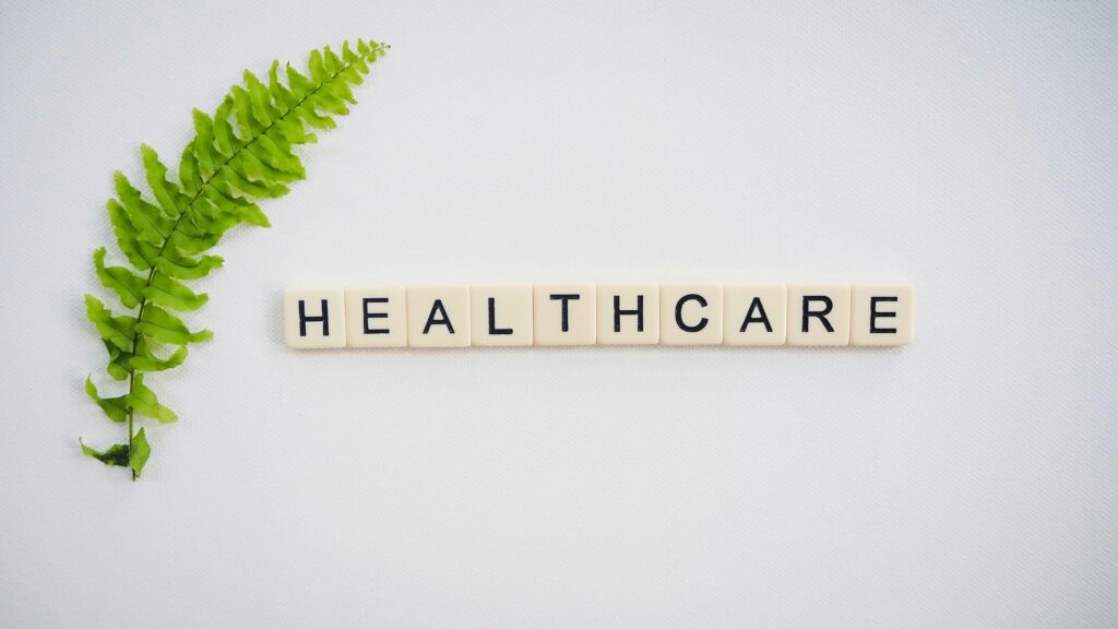 The word "healthcare " in scrabble letters. A leaf on the left side of the word. White background. 