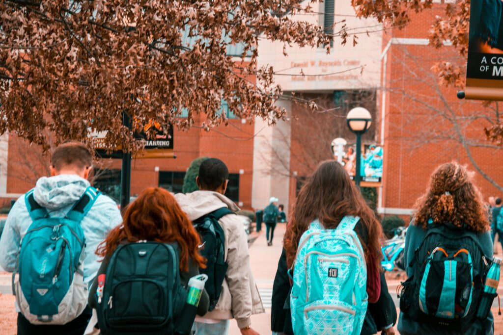 Young adults with backpacks walking towards school 
