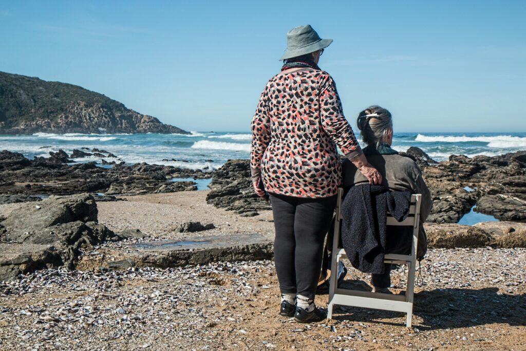 Oman standing next to lady in wheelchair on the beach