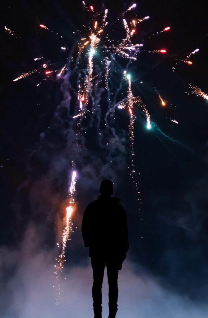 man standing in the dark, looking at fireworks