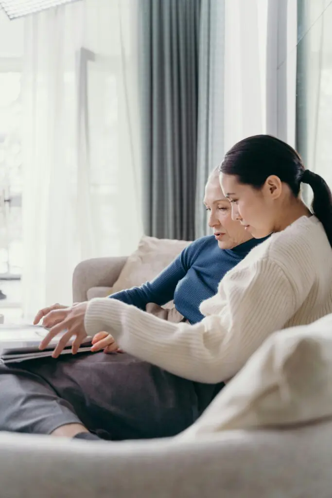 two women sitting on a couch. Side profiles. Overlooking a document. 