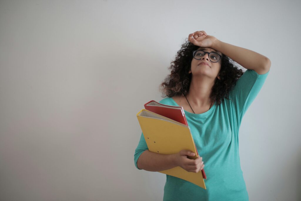 lady in blue shirt with her hand on her forehead, holding a yellow and a red notebook. 