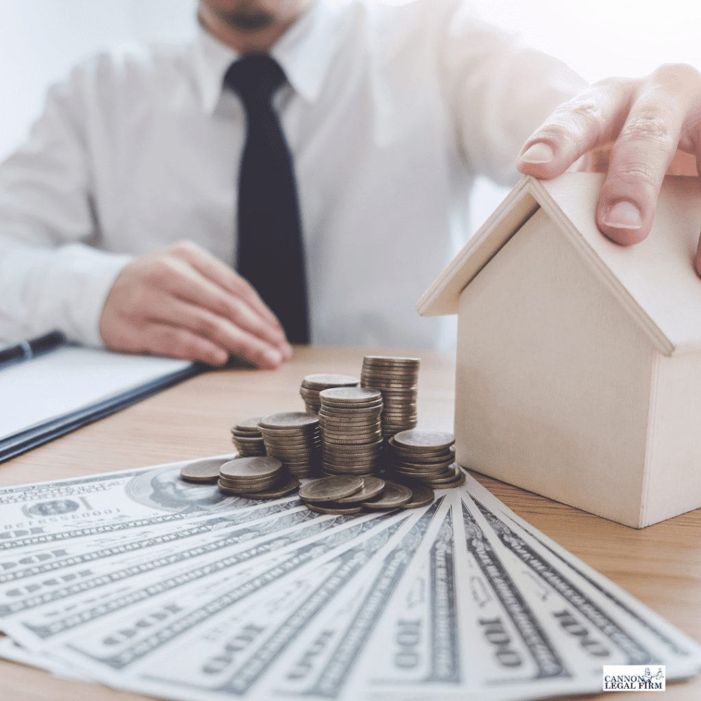 Money and coins laid on a table with a man's hands on a small wooden house for high-net-worth individuals
