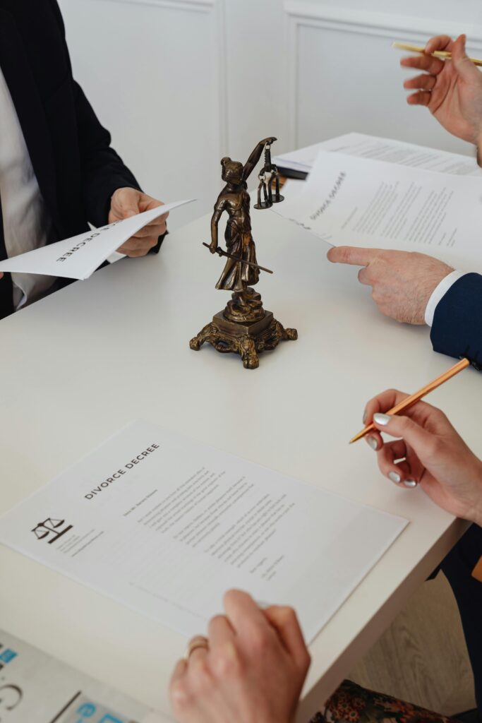 Lady justice figurine over a law office table. Three sets of hands hover over the table holding legal documents. 